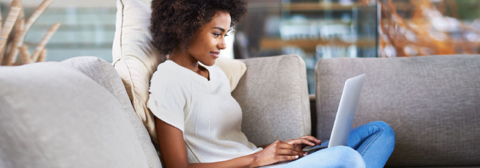 Smiling female using laptop at home to send cash online 