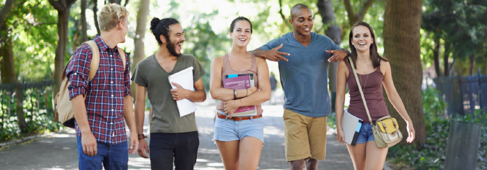 Ethnically diverse group of smiling students walking on college campus 