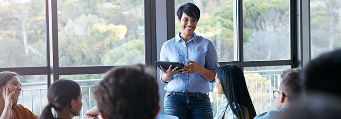 Smiling female teacher holding tablet in classroom with students