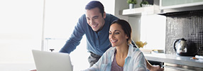 Smiling couple looking at laptop for checking account options 