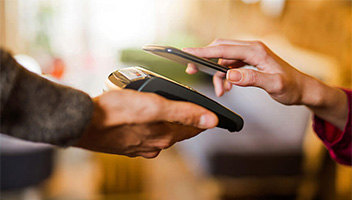 Hand holding credit card terminal and another hand holding mobile phone to pay and tap